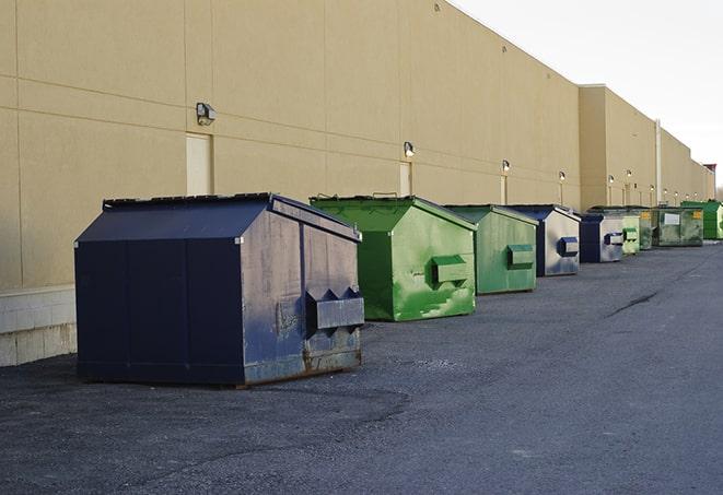 a construction worker unloading debris into a blue dumpster in Cohasset